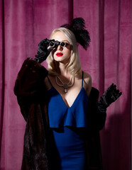 Blonde woman in vintage blue dress and fur coat with opera glasses