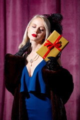 Fototapeta premium Blonde woman in vintage blue dress and fur coat with gift box