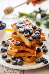 Waffles with addition of fresh blueberries sprinkled with castor sugar on a white plate close up view