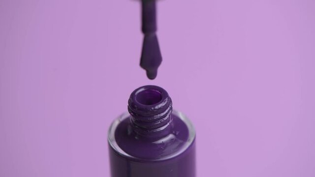 Close up of open nail polish. A drop of varnish is dripping from the brush.