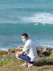 Naklejka na ściany i meble Man in white t-shirt and blue shorts, wearing a surgical mask on the seashore.