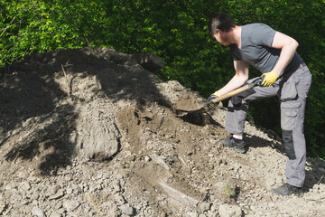 A man working with a shovel near a heap of soil.