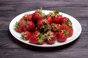 fresh strawberries on a white plate on a black wooden background