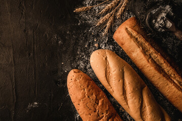 Variety of delicious breads and buns on dark slate background with wheat spikiletes, sackcloth. Pastries and bread in a bakery. Food concept, top view