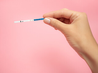 Female hand holding positive pregnancy test isolated on pink background. The abbreviation HCG on the blue bar means Human chorionic gonadotropin is a hormone produced by cells that are surrounding a