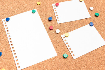 Perspective view of blank papers on a cork board with multi colored thumb tacks around