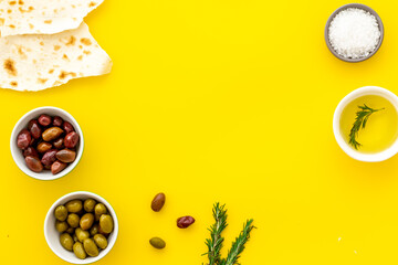 Top view of olives, olive oil, bread on yellow table top view copy space