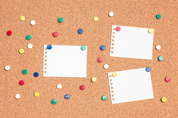 Flat lay of blank papers on a cork board with multi colored thumb tacks around
