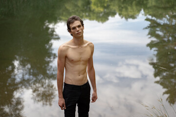 Portrait of shirtless man standing against lake in forest
