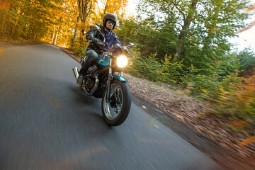 Motorcycle driver riding in autumn forest, blur motion effect