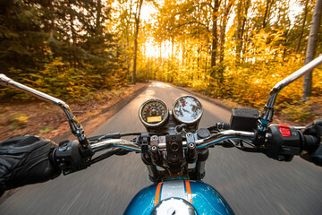 Motorcycle driver riding in autumn forest, handlebars view