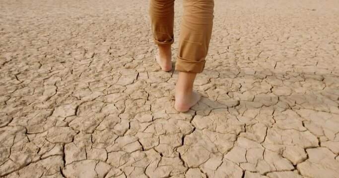 Close up shot of feet of adult man walking barefoot on bottom of dried lake or river, stepping on cracked soil ground destroyed by erosions - ecological issues concept 4k footage