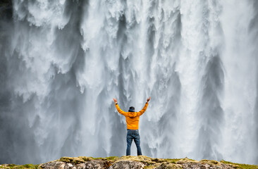Man admirnig the beauty of iconic Skogafoss waterfall in Iceland, Europe.