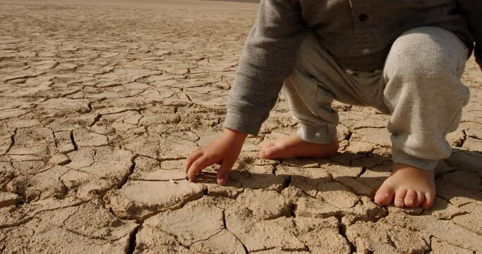 Close up shot of baby boy poking pieces of dry cracked mud. Cracked soil ground of dried lake or river destroyed ny global warming - ecological issues 4k footage