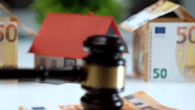 Real estate auction according to the law. Stack of money falling on the table and judge banging gavel on paper currency. Luxury house is sold already, house ownership concept