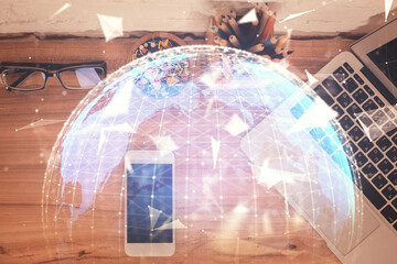 Double exposure of business theme hologram over desktop with phone. Top view. Mobile international...