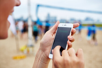 A woman adjusts the volume of music playing from her smartphone during outdoor sports activities at the beach with friends.