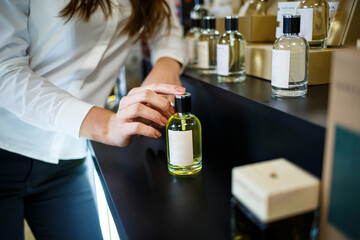 Bottle perfume female hand. Young woman holding bottle of perfume. Fashionable perfumes in hands of women. Girl sprays perfume. Beautiful women's hands.