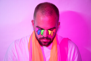Sad homosexual young man with colorful pink lights and his face painted