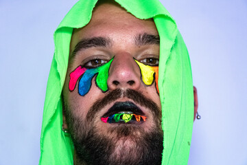 Portrait of a man with colors and green hood. Lgbt young boy with painting face