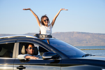 Asian woman in car with raised hands driving on sunset