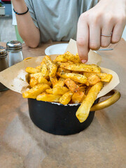 Close-up of a female young woman taking a fried potatos with oregan placed on a pan on a table. Greek food culture.