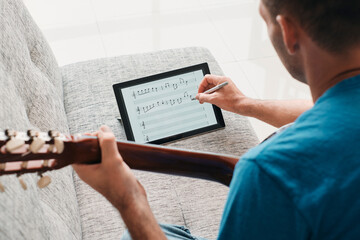 Man Composing Acoustic Guitar Sheet Music On Digital Tablet