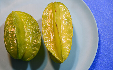 Two carambola fruits on green color plate on blue background