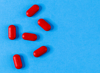 Six red pills are scattered to the left against a blue background and with space for text on the right, top view close-up.