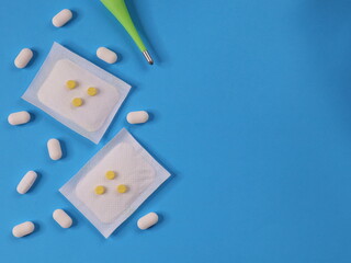 A tempometer, various pills and medical powder in sachets lie on the left against a blue background...
