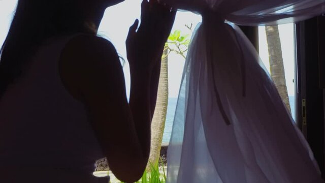 Girl in morning in the bed with white bedsheets and curtains in bungalow on sea cite on island