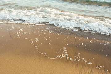 Soft beach sand with an incoming foam wave.