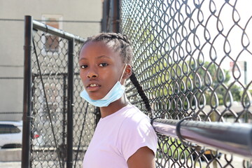 African American Preteen wearing surgical face mask outdoors in urban park close up fence background