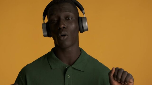 Handsome stylish African American guy in headphones emotionally singing and dancing on camera over colorful background