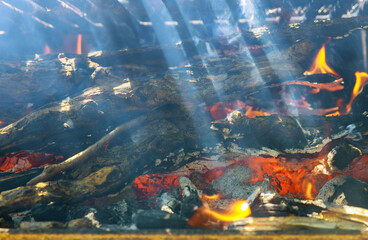 Fototapeta na wymiar Ray of sunshine through burning firewood metal grill. Soft focus.