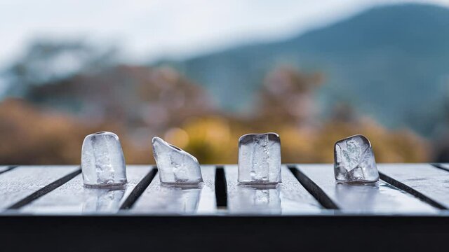 Melting ice cubes on a wooden table on a balcony on a mountain and sunset background in autumn. 4K time-lapse