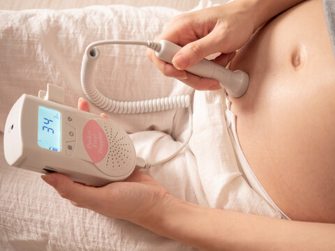 Asian Woman Using Pocket Fetal Doppler To Monitor Baby Heart Beat. Expectant Mother Happy And Smile When Examine Belly.