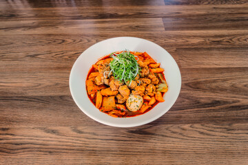 Korean Chicken and Green Onion Tteokbokki at a 45 degree angle on a wood table in a white bowl.