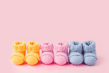 Fototapeta na wymiar Pregnancy motherhood perenthood concept, Three pairs of baby booties on pink background, baby shower, first birthday party banner, handmade socks, daycare, kindergarten, day nursery