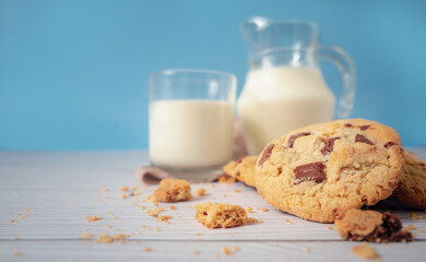 Delicious homemade chocolate chip cookies, paired with fresh milk in a glass and pitcher, placed on a white wooden floor and a blue background cloth. Drink in the morning for health and strong bones.