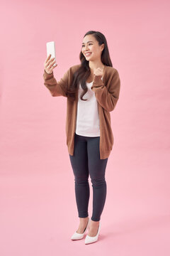 Portrait of an attractive young asian woman using mobile phone while standing with copy space over pink background