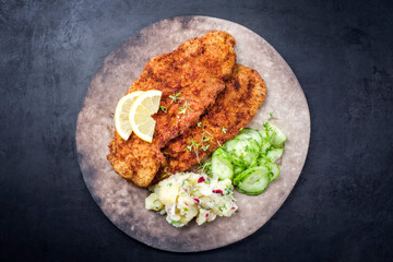 Traditional deep-fried schnitzel with potato and cucumber salad offered as top view on a rustic...