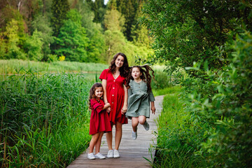 Obraz premium Family portrait of a large friendly family. A Caucasian pregnant mother and two children stand together in a Park on a wooden bridge. A young pregnant mother with a family in the countryside.