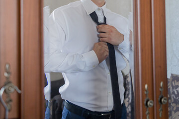 a man puts on a tie in front of a mirror