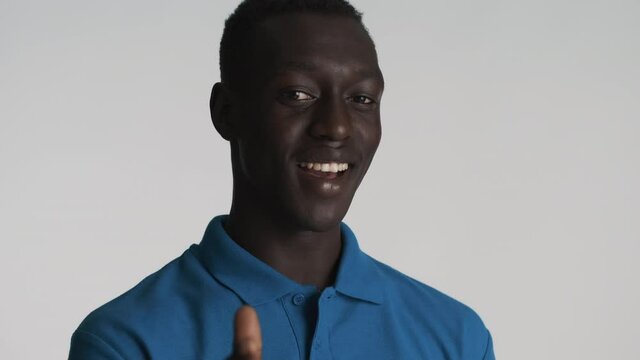 Cool African American guy happily winking on camera pointing at you gesture over gray background
