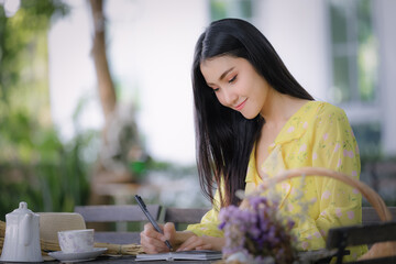 young asian woman hand is writing on notepad with a pen in the garden .