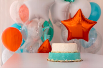 Delicious birthday cake with white and blue frosting placed on table on background of colorful helium balloons