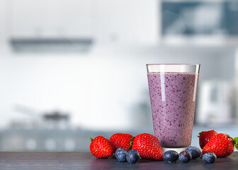 glass of smoothie and berries on table in front of blurred kitchen
