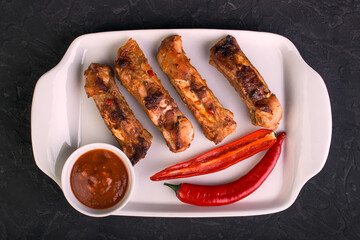 Sliced baked pork ribs on a white plate with hot pepper and red sauce