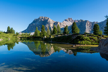 Fototapeta na wymiar Panoramic view of idyllic summer landscape in the Alps with clear mountain lake and fresh green mountain pastures in the background